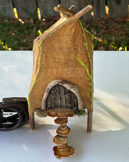 Image of gnome house made of sticks and paper on white table.